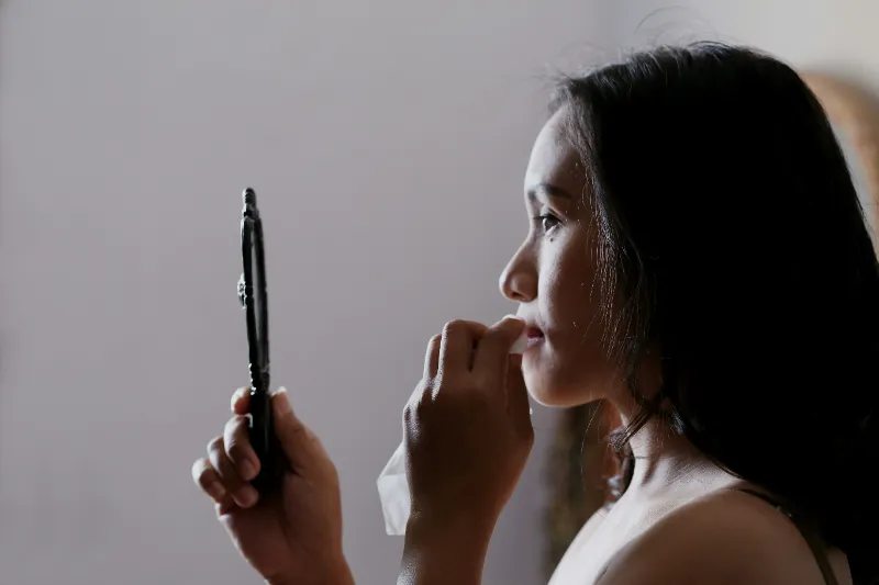 A woman in a black dress looks at herself in the mirror