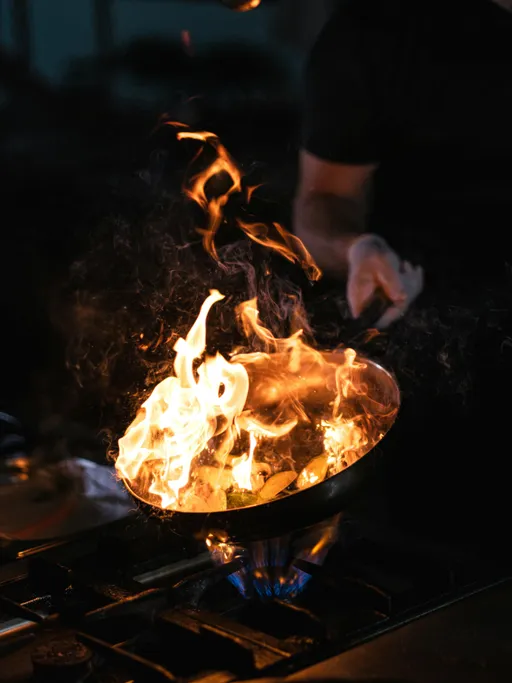 A skillet held over a stove with roaring flames burning food in the skillet
