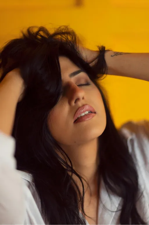 A woman running her hands through her hair with an ambiguous expression on her face. She may be feeling relaxed, ecstatic, or frustrated.