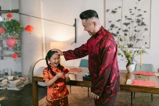A middle-aged man in red attire putting his hand on the head of a young girl. The girl is smiling in delight.