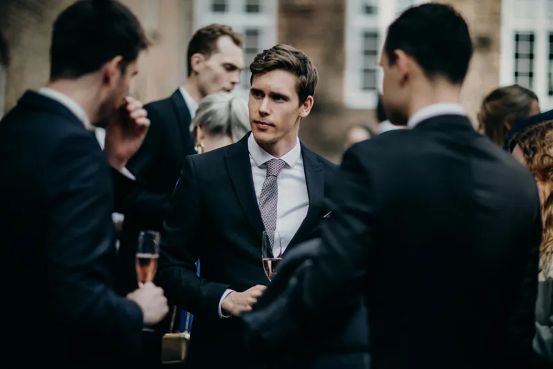 Three men in suits talking at a party. One is looking intently as the others speak.