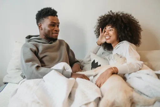 Whimsical couple in bed—one drawn as a mischievous demon, the other a gentle angel, both smiling knowingly